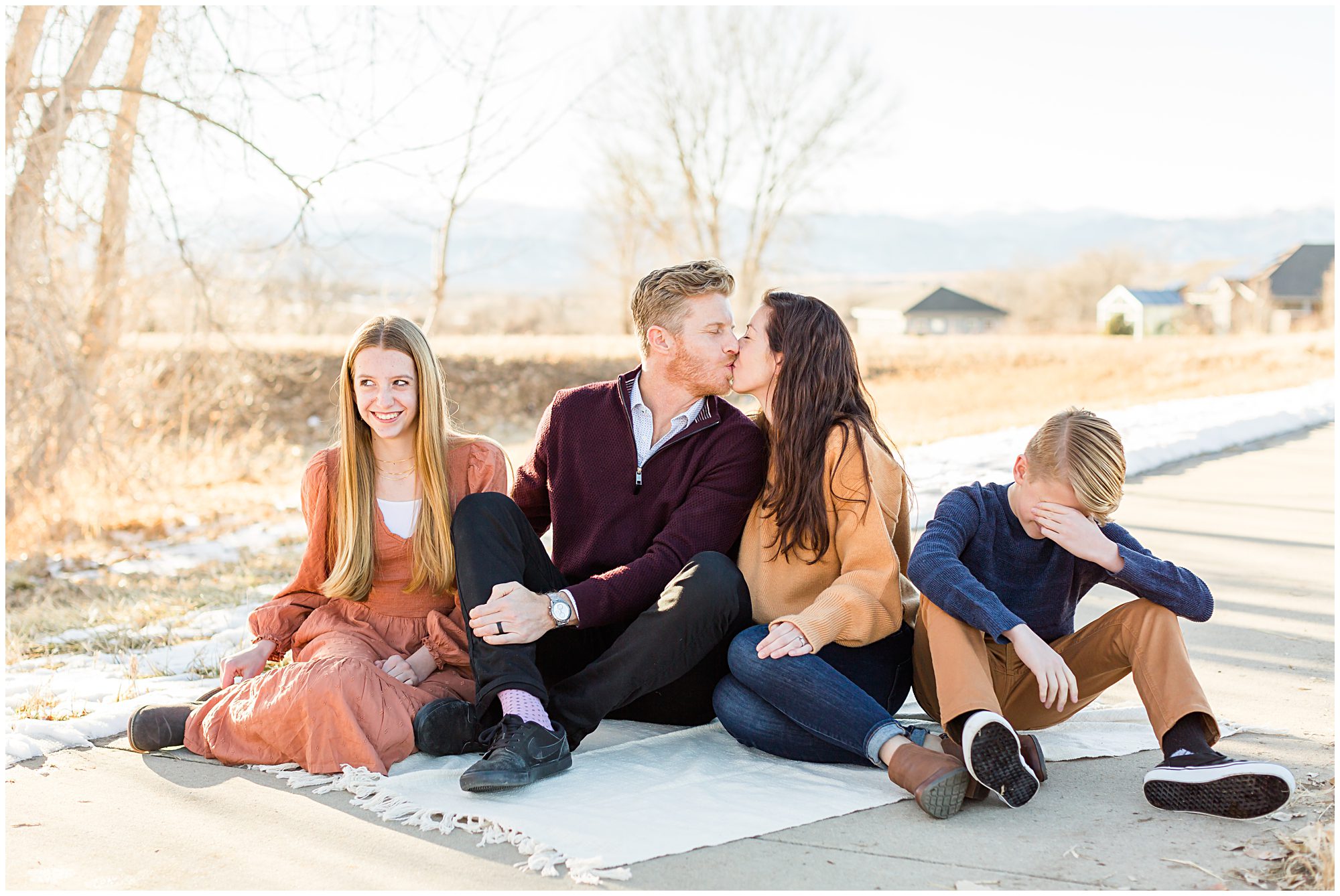 A husband and wife share a kiss to the embarrassment of their teenage children during an outdoor family portrait session in Erie Colorado