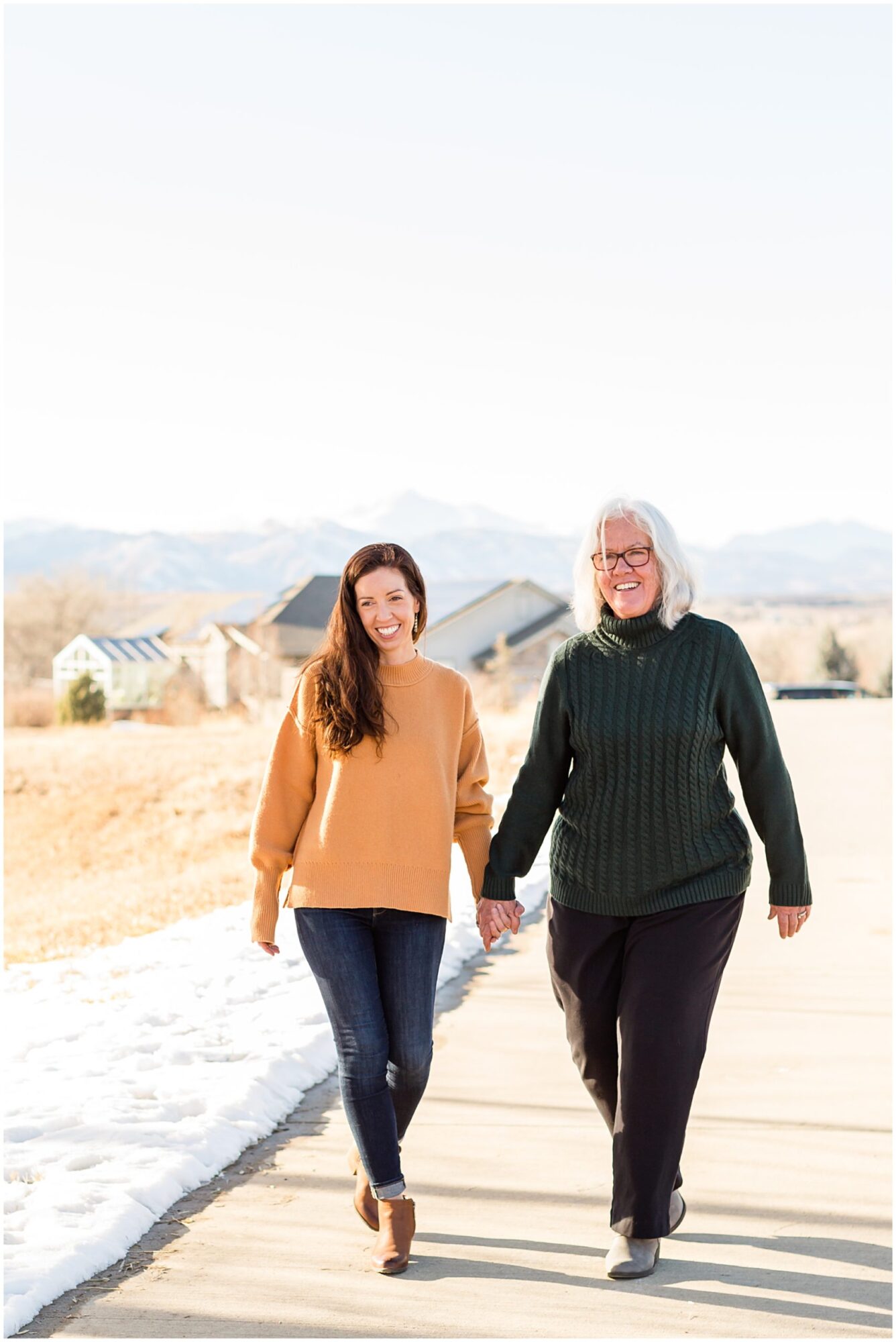 A mother and her grown daughter hold hands while walking along a trail during an outdoor family session in Erie Colorado