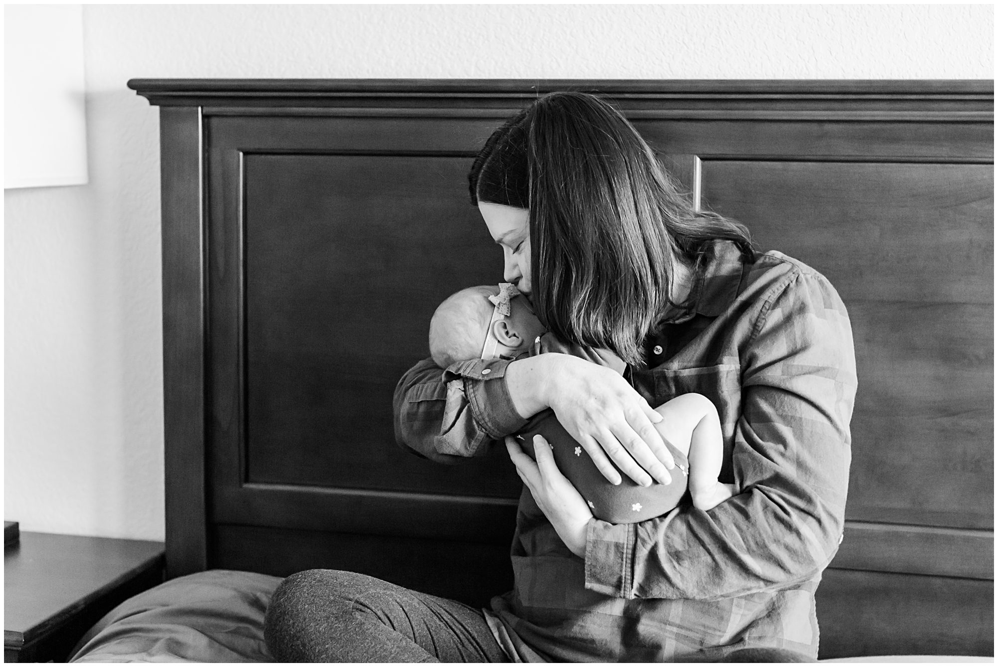 A mother kisses her newborn baby on the temple while cradled in her arms