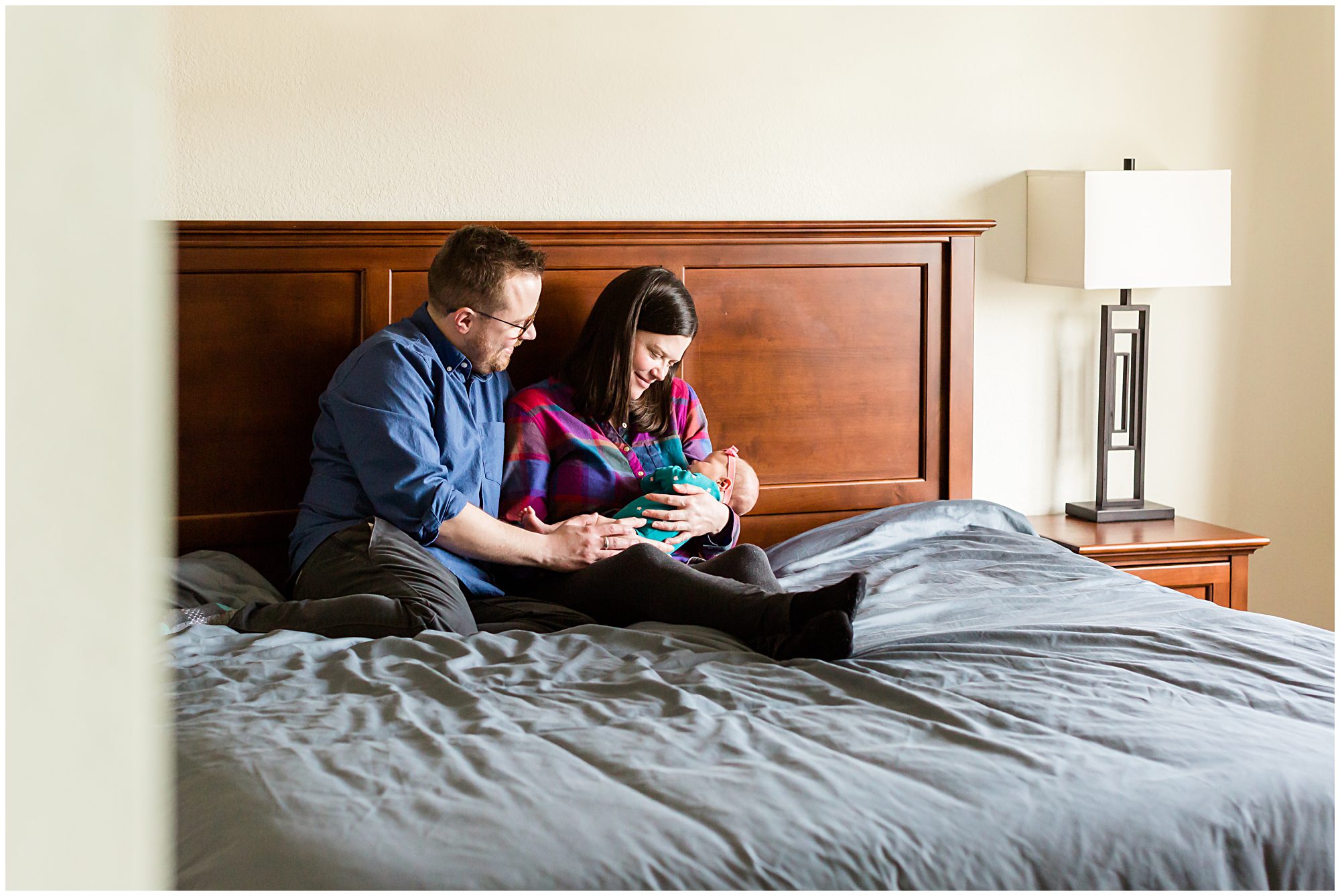 A mother and father snuggled on a bed gaze adoringly at their newborn baby