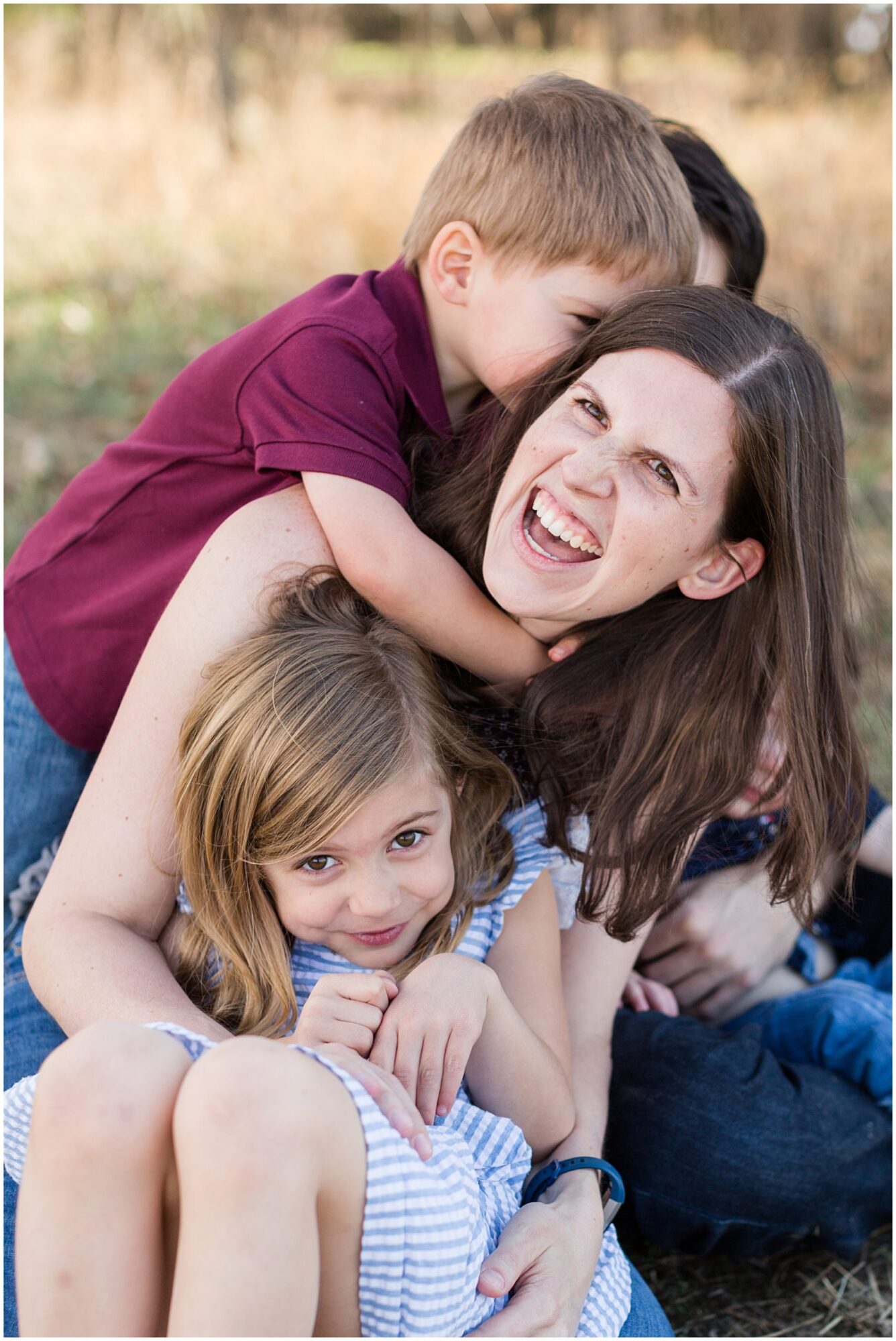 A young mother laughs at the camera as her son surprises her with a hug from behind during an outdoor family portrait session in Erie Colorado