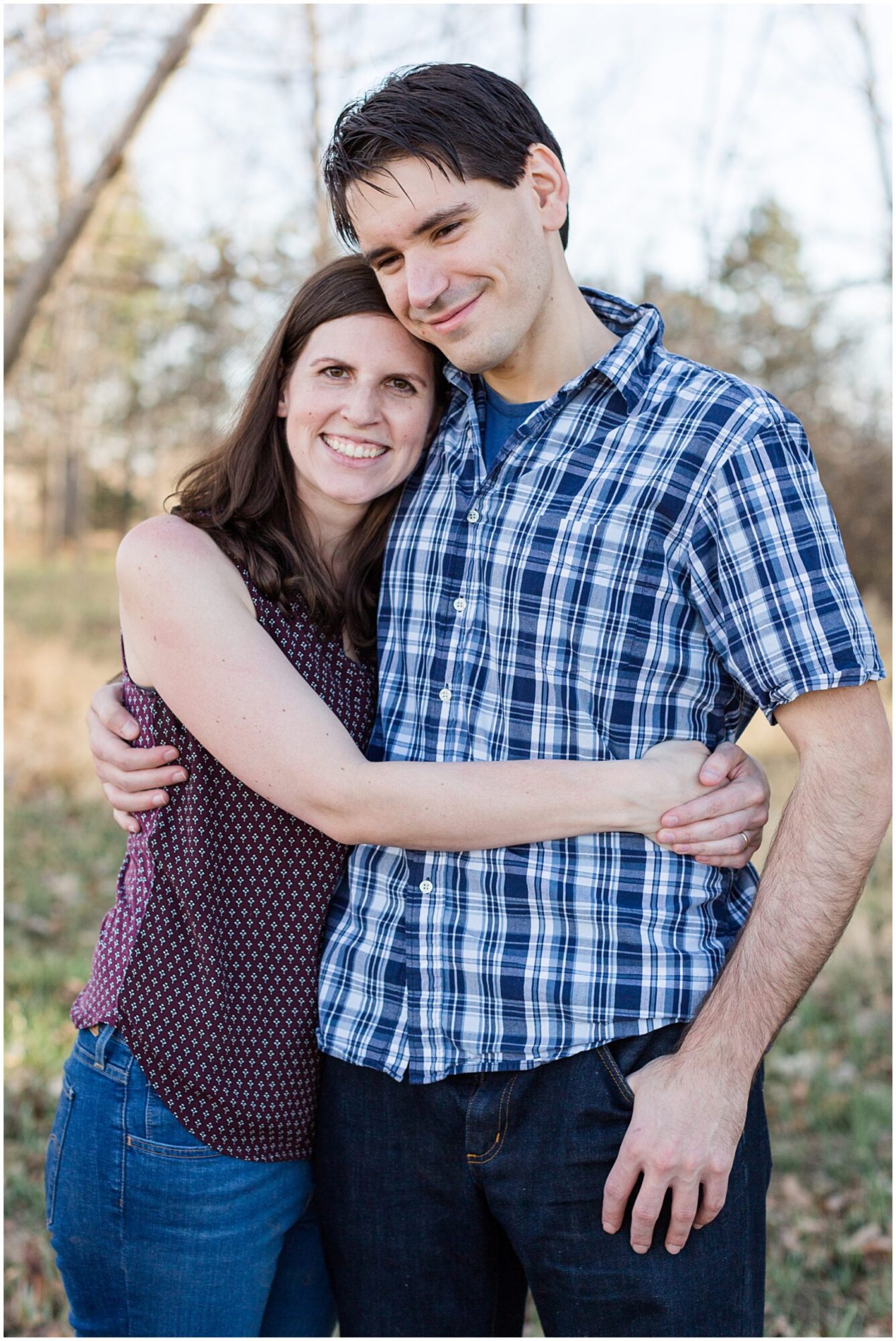 A young husband and wife smile at the camera as they embrace during an outdoor family photo session in Erie Colorado