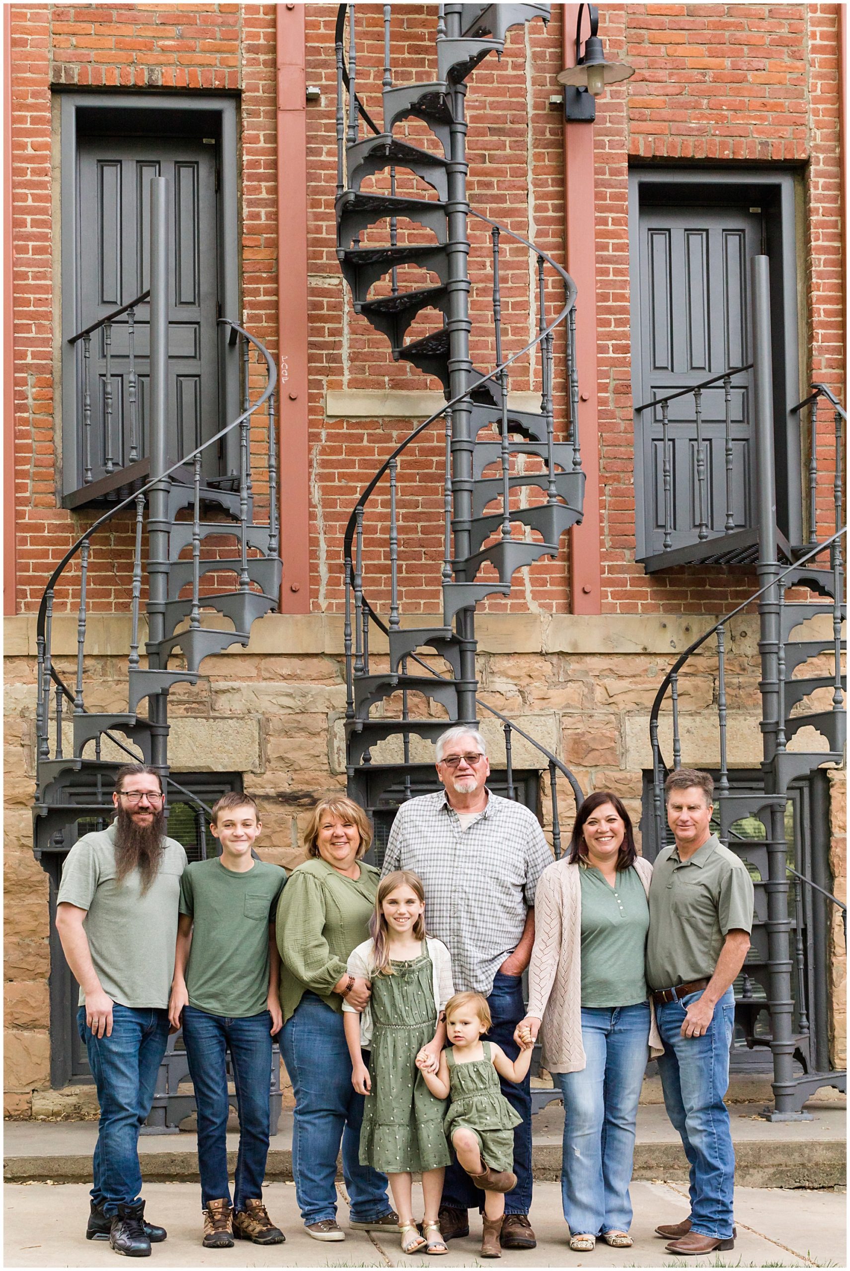 An extended family posed in front of a trio of curved iron staircases smile at the camera 
during a family photo session in Boulder