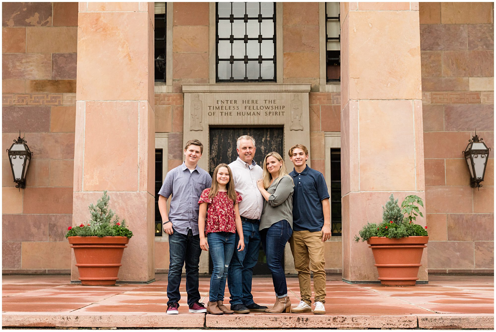 A mother, father, and their three teenage children pose in front of a historic building and smile at the camera during their family portrait session