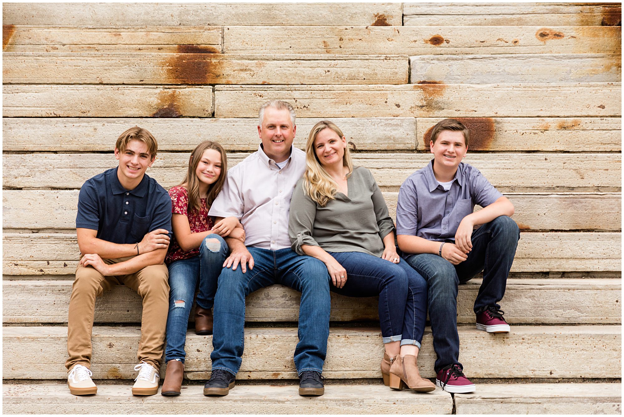 A mother, father, and their three teenage children smile at the camera during their family portrait session in Boulder