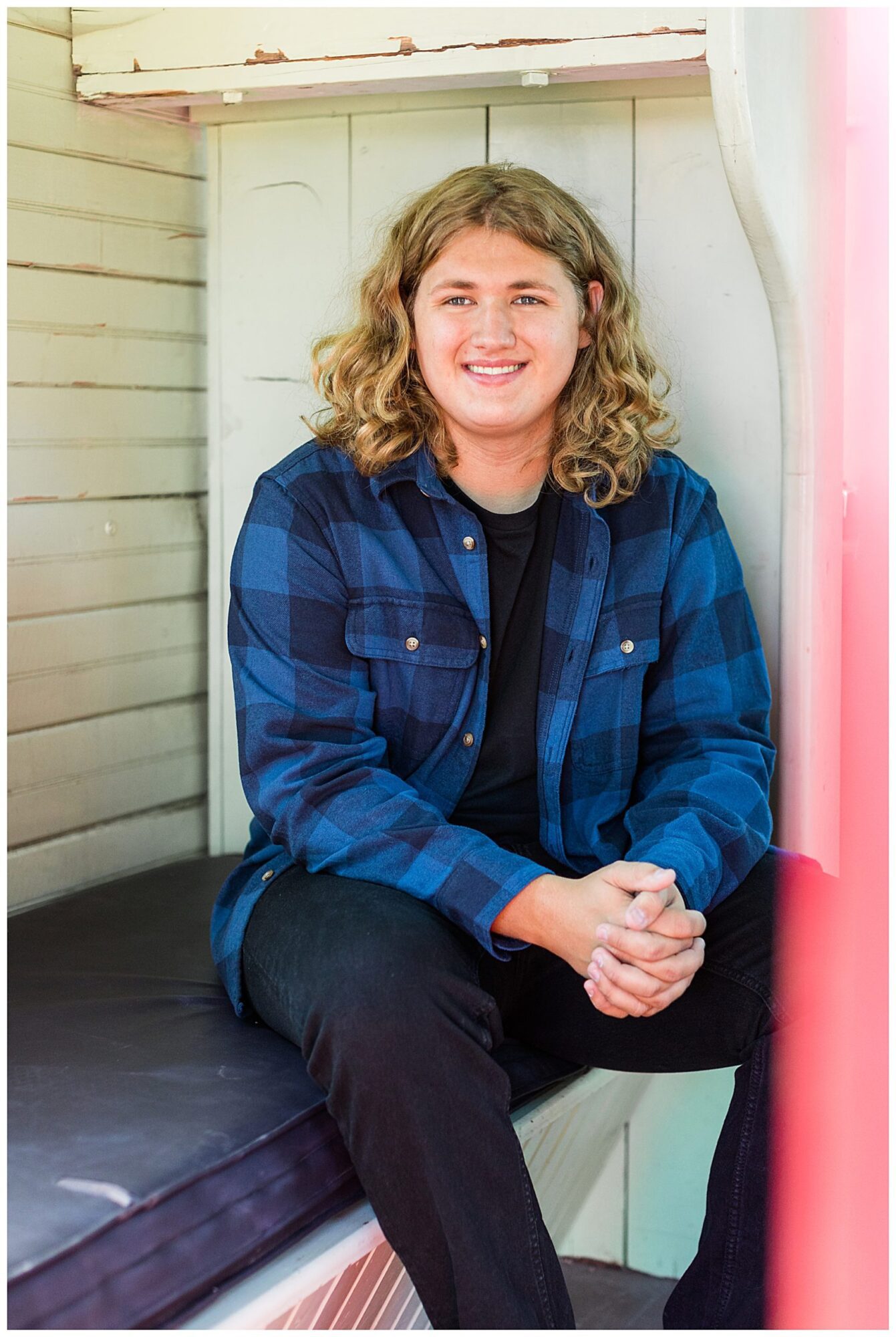 A high school senior guy poses on a bench inside an old train during his senior portrait session