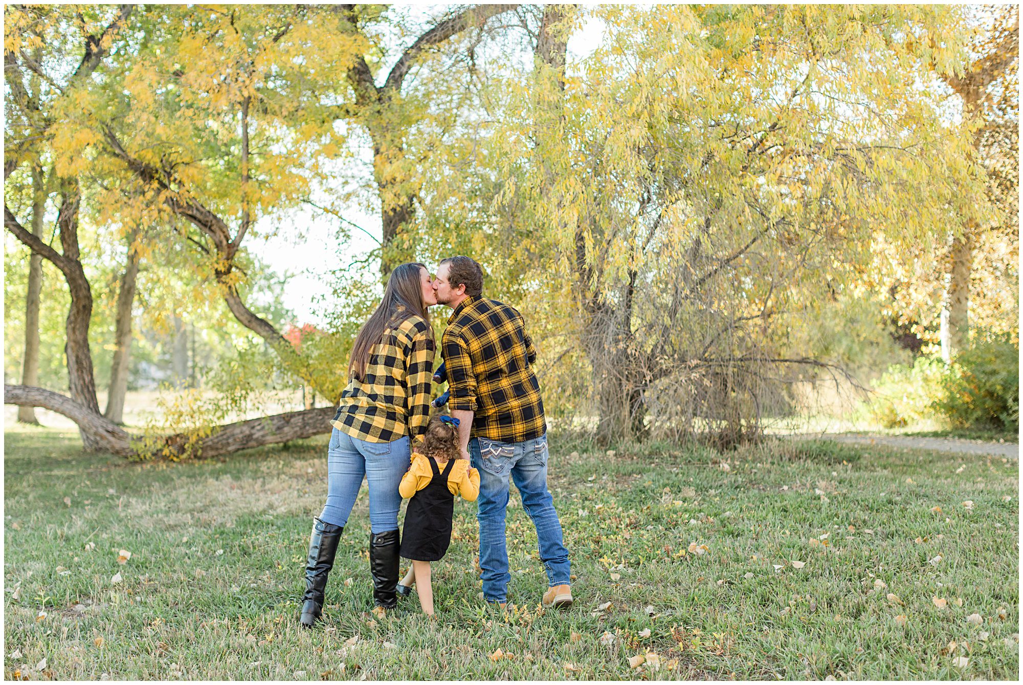 A mother and father share a kiss as they hold their daughter's hands during their family mini session at Thomas Reservoir