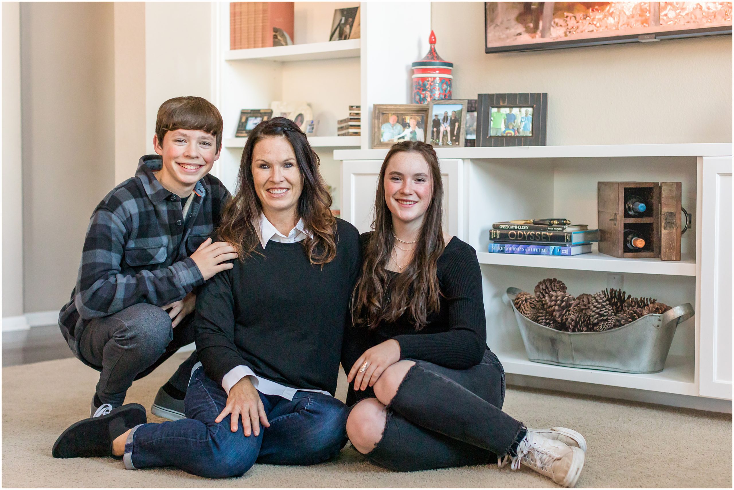 A mother and her teenage son and daughter snuggle together on the floor in their living room during an extended family session