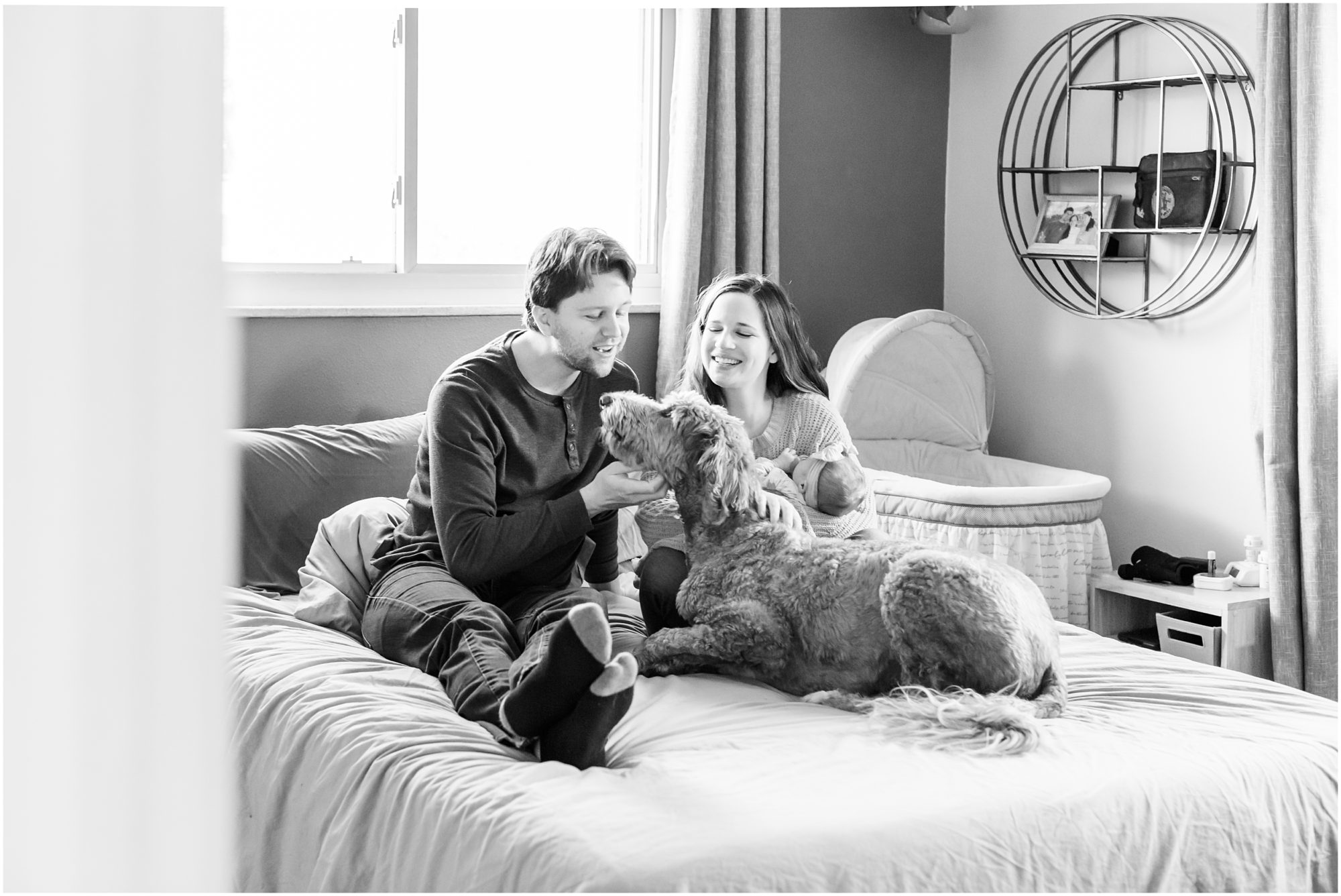 A candid photo of a new mom and dad relaxing on their bed with their baby girl and dog taken during their in-home newborn session by Theresa Pelser Photography