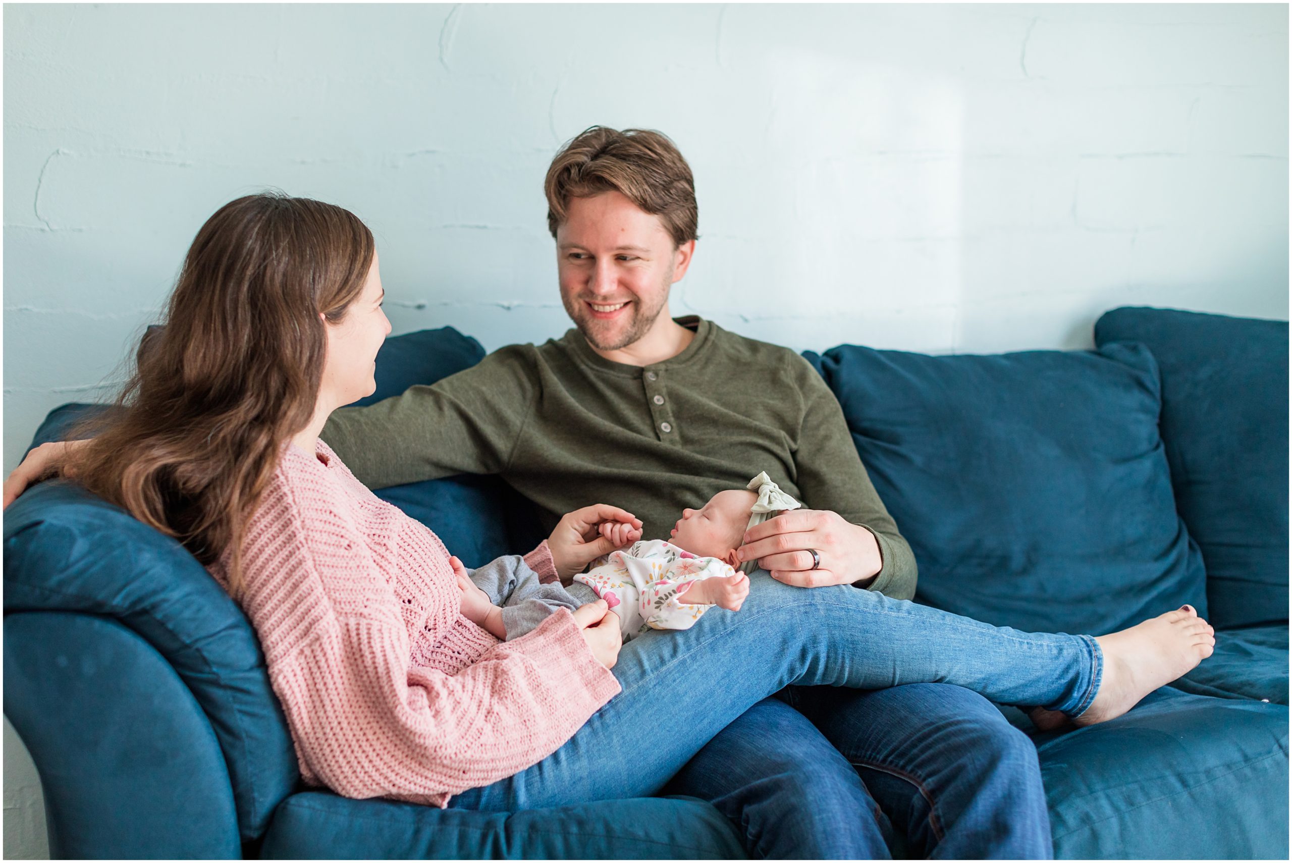 A candid photo of a new mom and dad relaxing on a sofa with their baby girl taken during their in-home newborn session by Theresa Pelser Photography