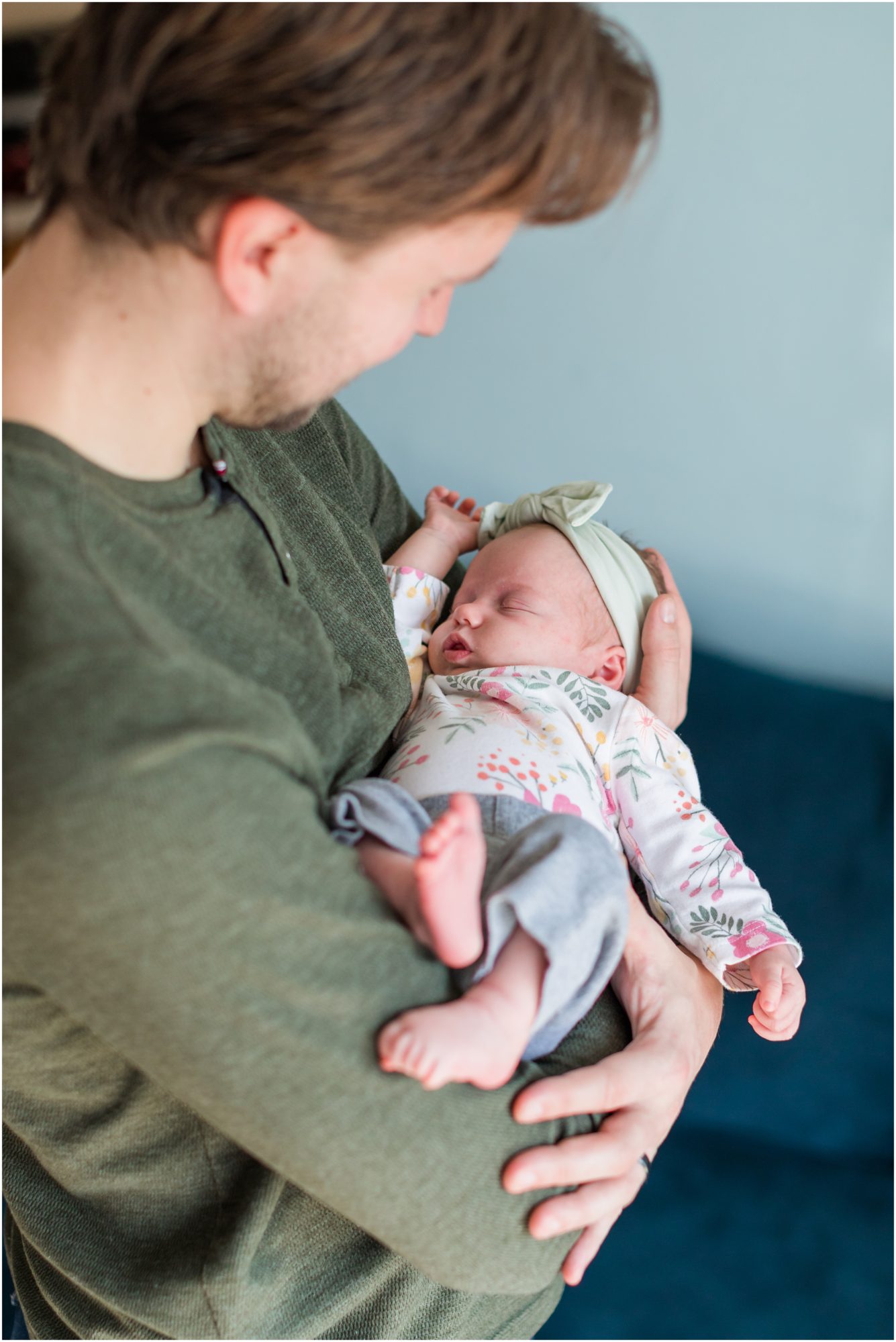 A photo a new dad cradling his sleeping baby girl during an in-home newborn session by Theresa Pelser Photography