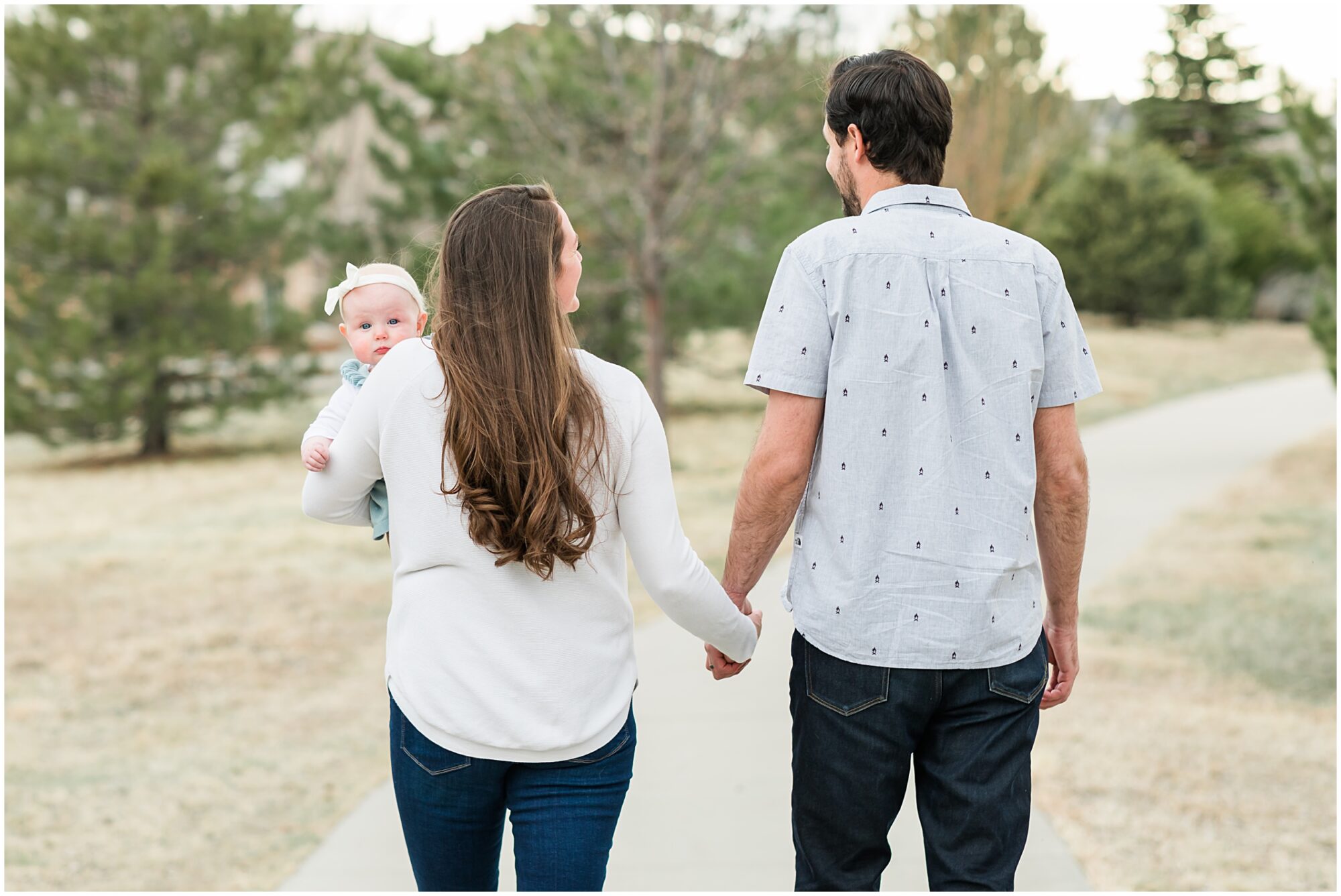 A photo of mother and father walking hand in hand as their baby girl peers over her mother’s shoulder towards the camera captured during their family session with Theresa Pelser Photography