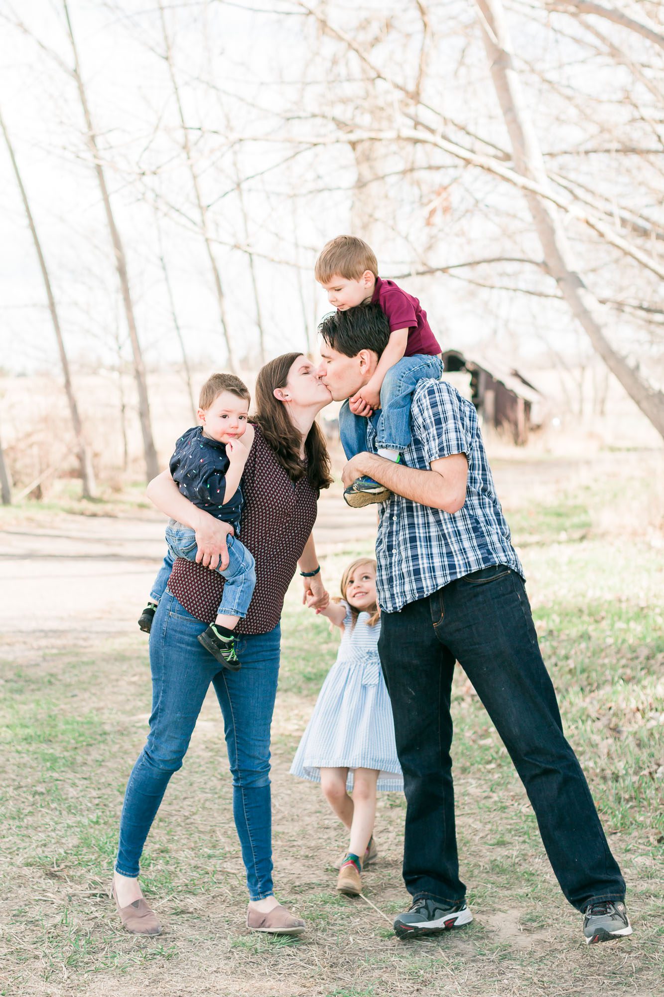 Family of five enjoying a playful moment outdoors, with parents kissing while holding their children, during a family photo session in Erie, Colorado.