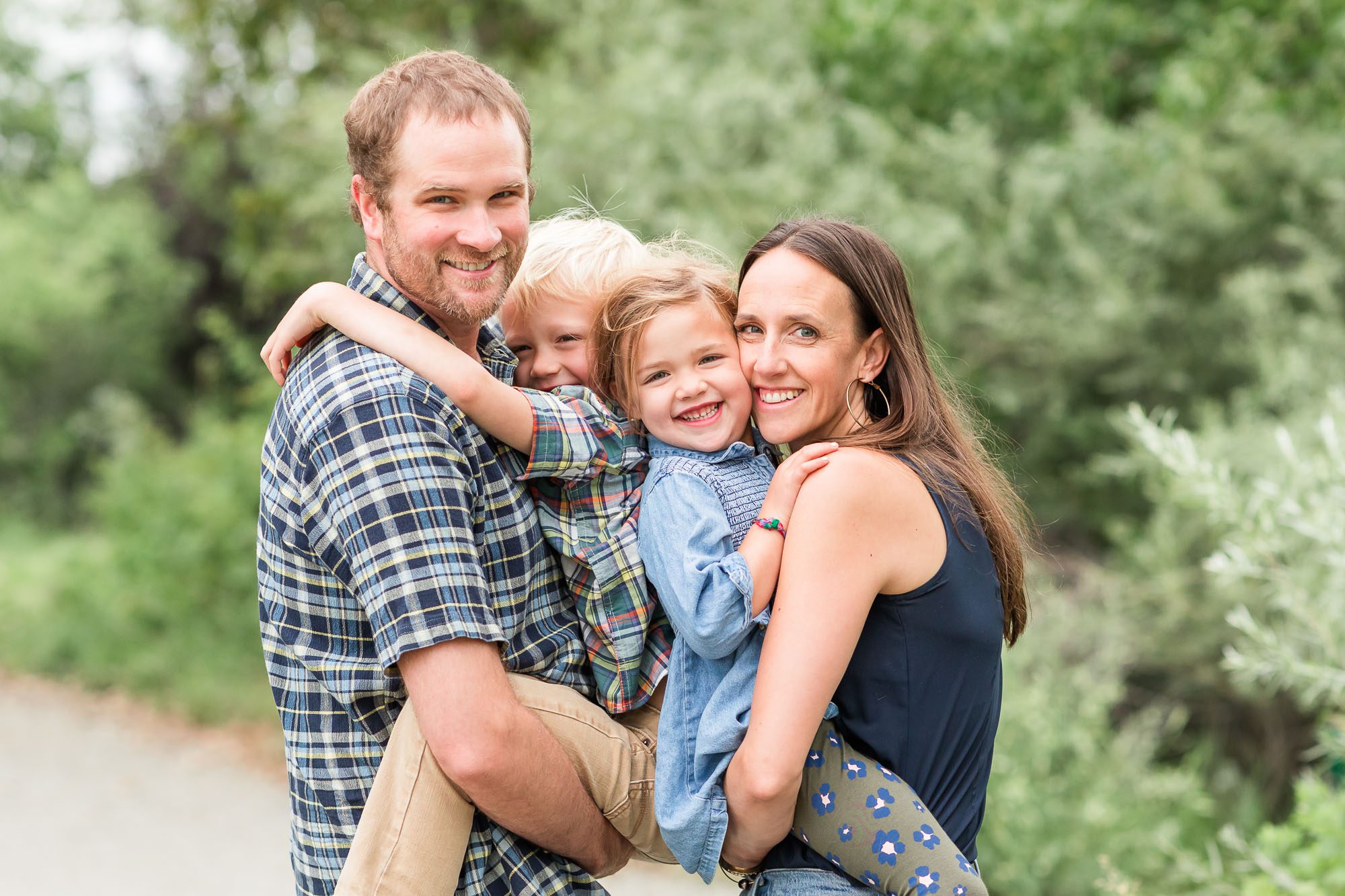 Outdoor family photo with parents smiling and holding their two young children, taken by an Erie family photographer.