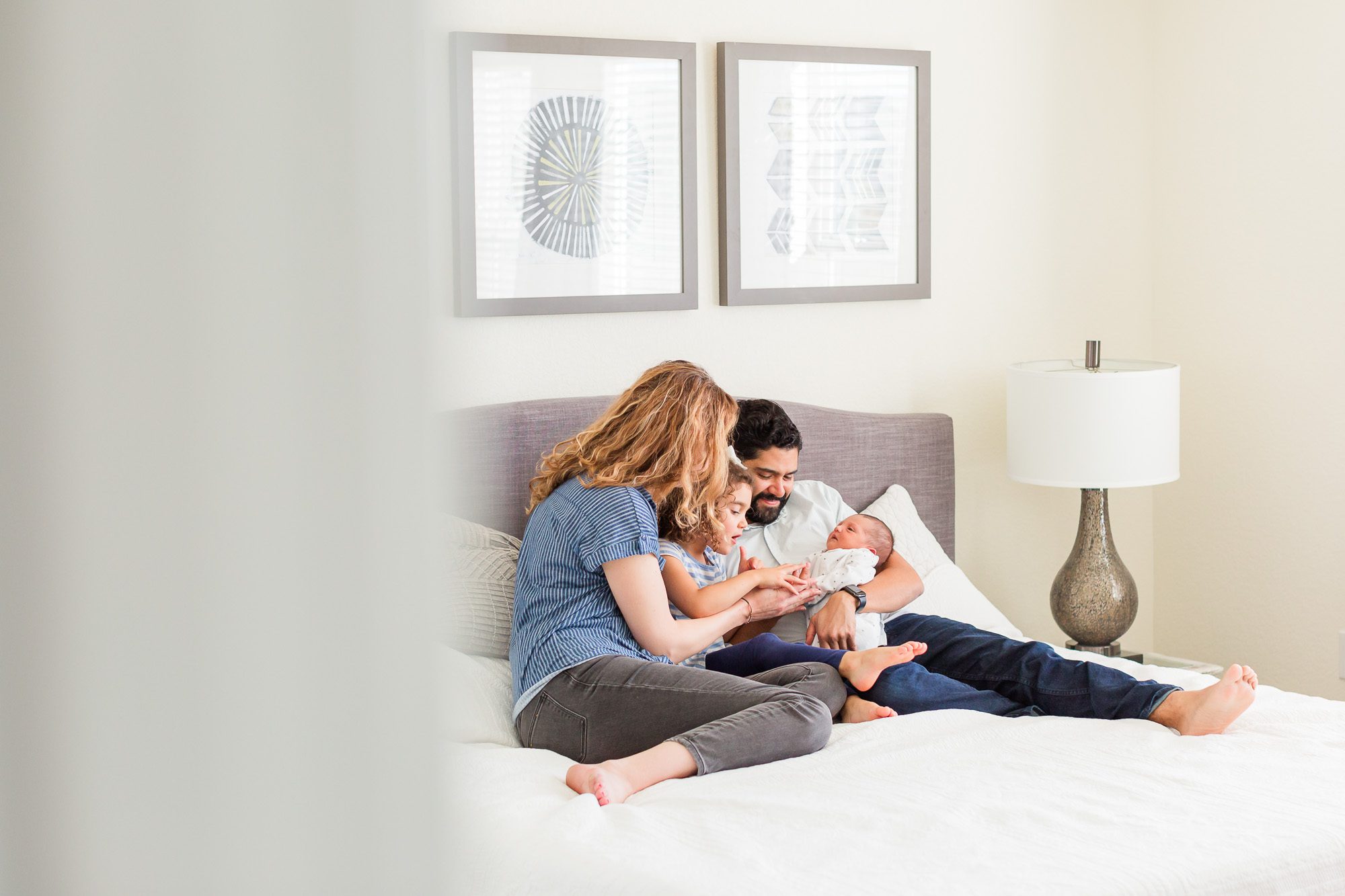 Family sitting together on a bed during a newborn photo session, with parents and a sibling gently holding the baby, captured by an Erie family photographer.