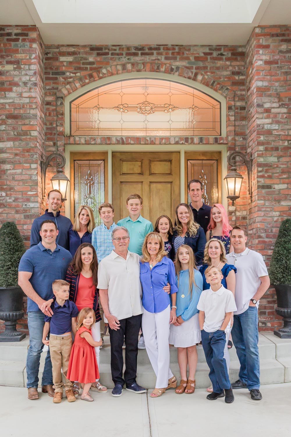 Extended family photo taken in front of a brick home during an at-home session in Niwot, Colorado—three generations smiling and gathered together on the front steps. Captured by Theresa Pelser, Colorado family and extended family photographer.