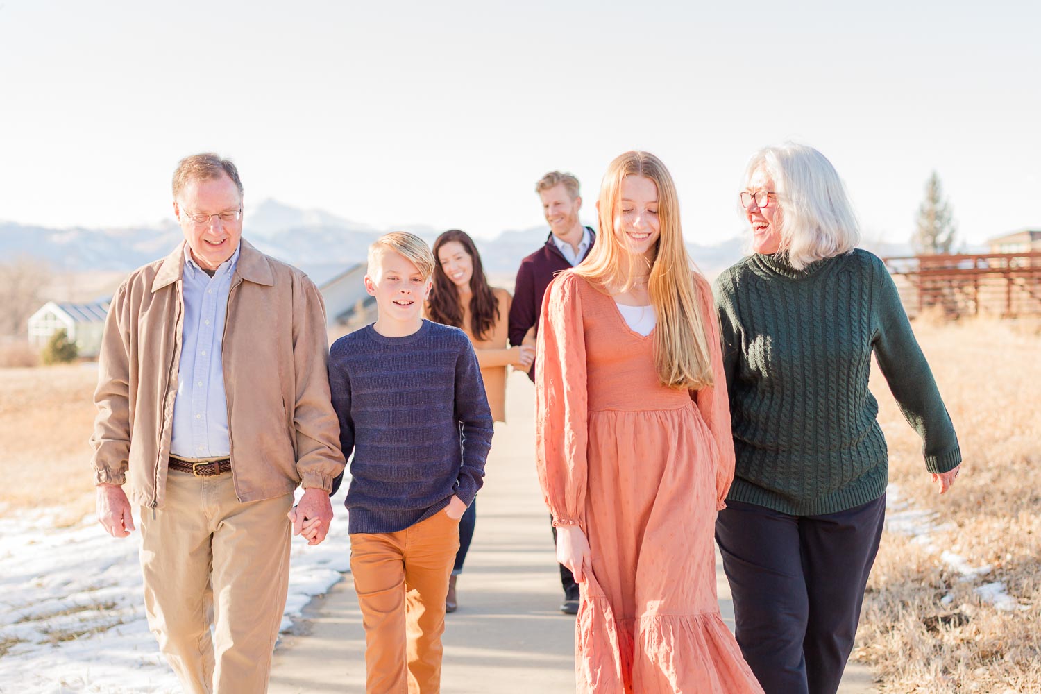 Extended family walking together during a sunny winter session in Erie, Colorado—captured on a path with mountain views and golden grass in the background. Photographed by Theresa Pelser, Erie family and extended family photographer.