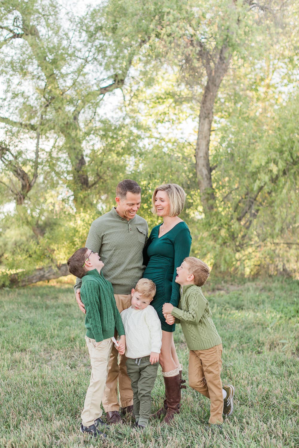 Fall mini session at Thomas Reservoir in Erie, Colorado—parents and their three young sons sharing a joyful, connected moment in a grassy field surrounded by trees. Captured by Theresa Pelser, Erie family photographer.