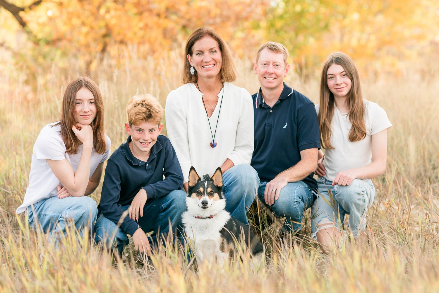 Fall mini session in Erie, Colorado—family of five with their dog sitting in a golden field surrounded by autumn colors, sharing a relaxed and happy moment. Captured by Theresa Pelser, Erie family photographer.