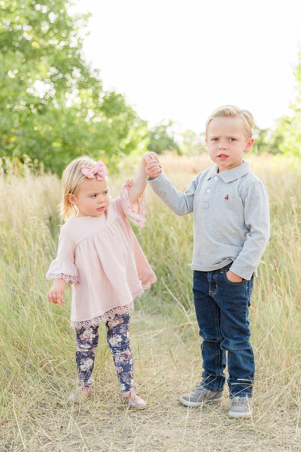 Fall mini session at Coal Creek in Erie, Colorado—young brother and sister holding hands and standing in a golden grassy field on a sunny afternoon. Captured by Theresa Pelser, Erie family photographer.