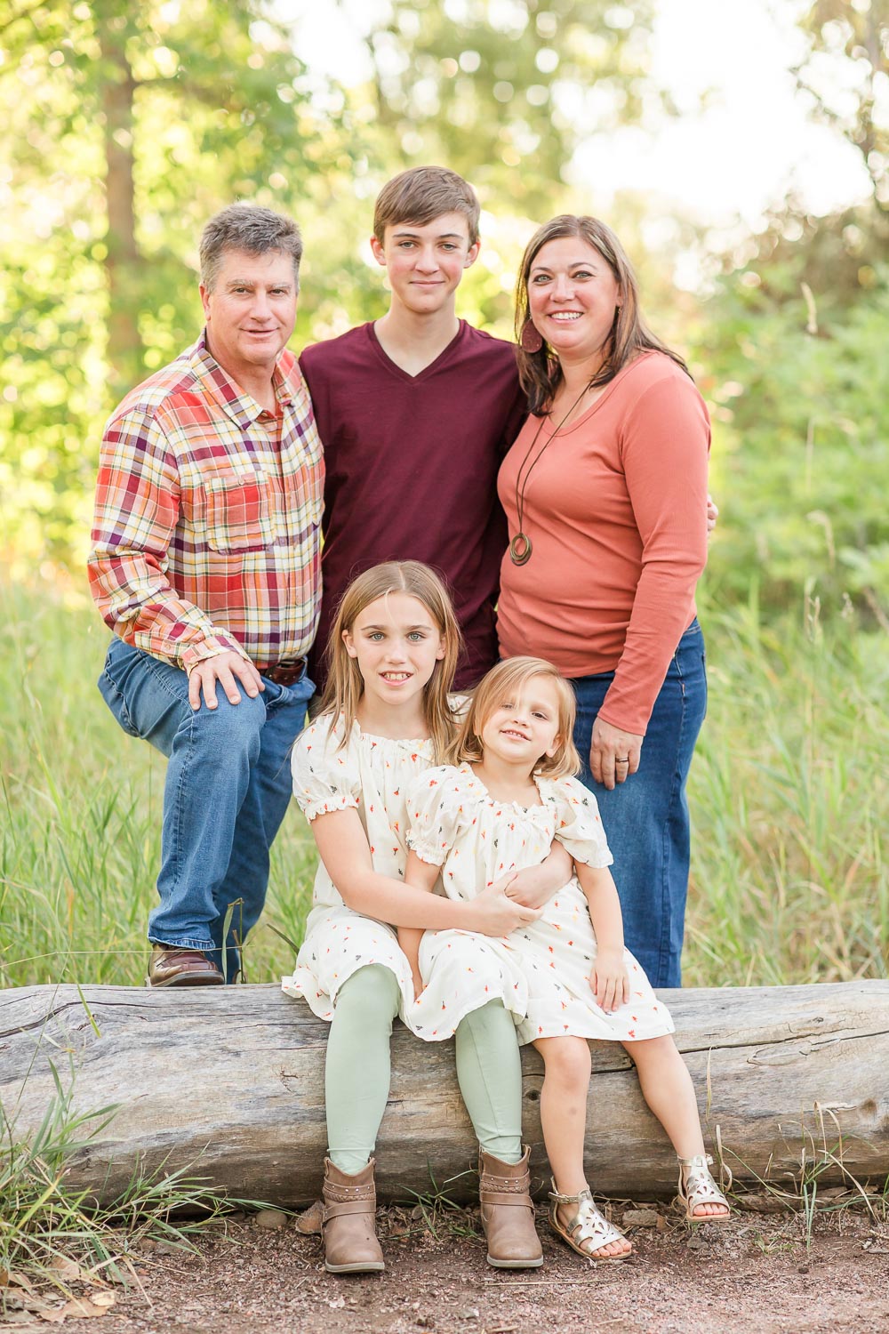 Fall mini session at McKay Lake in Thornton, Colorado—family of five posing together near a log in a sun-dappled field, dressed in warm autumn tones. Captured by Theresa Pelser, Thornton family photographer.