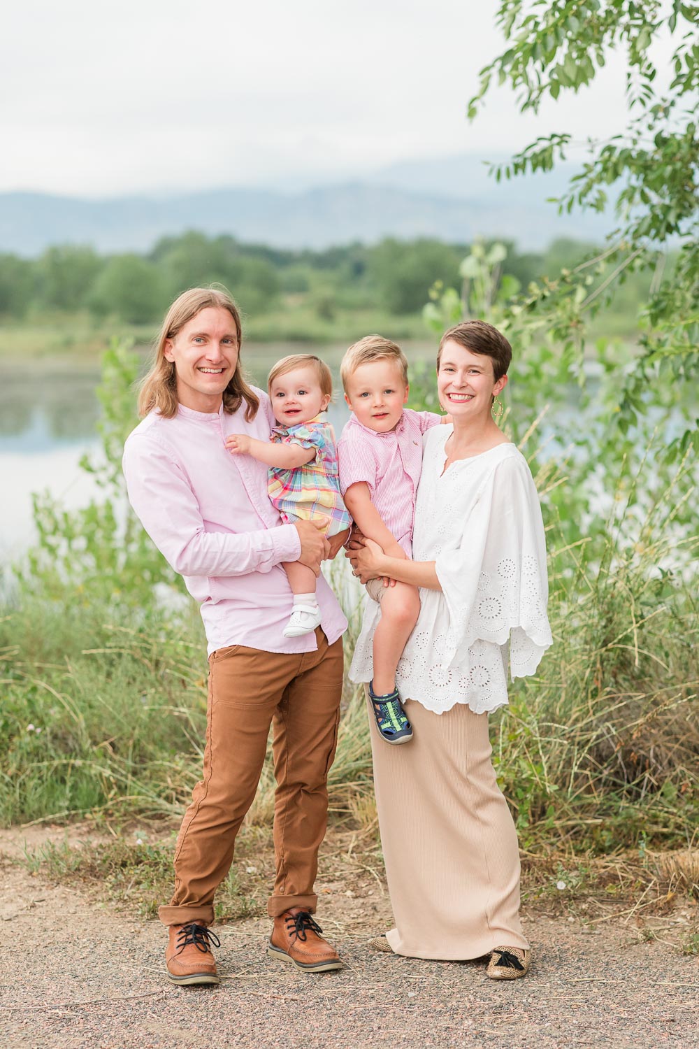 Family session at Walden Ponds in Boulder, Colorado—two parents and their young child smiling together near the water with mountain views in the background. Captured by Theresa Pelser, Boulder family photographer.