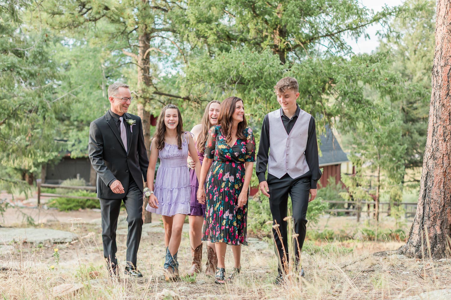 Family session at the Red Barn in Evergreen, Colorado—three teens and their parents walking together through a forested area, dressed in semi-formal outfits with smiles and laughter. Captured by Theresa Pelser, Erie family photographer.