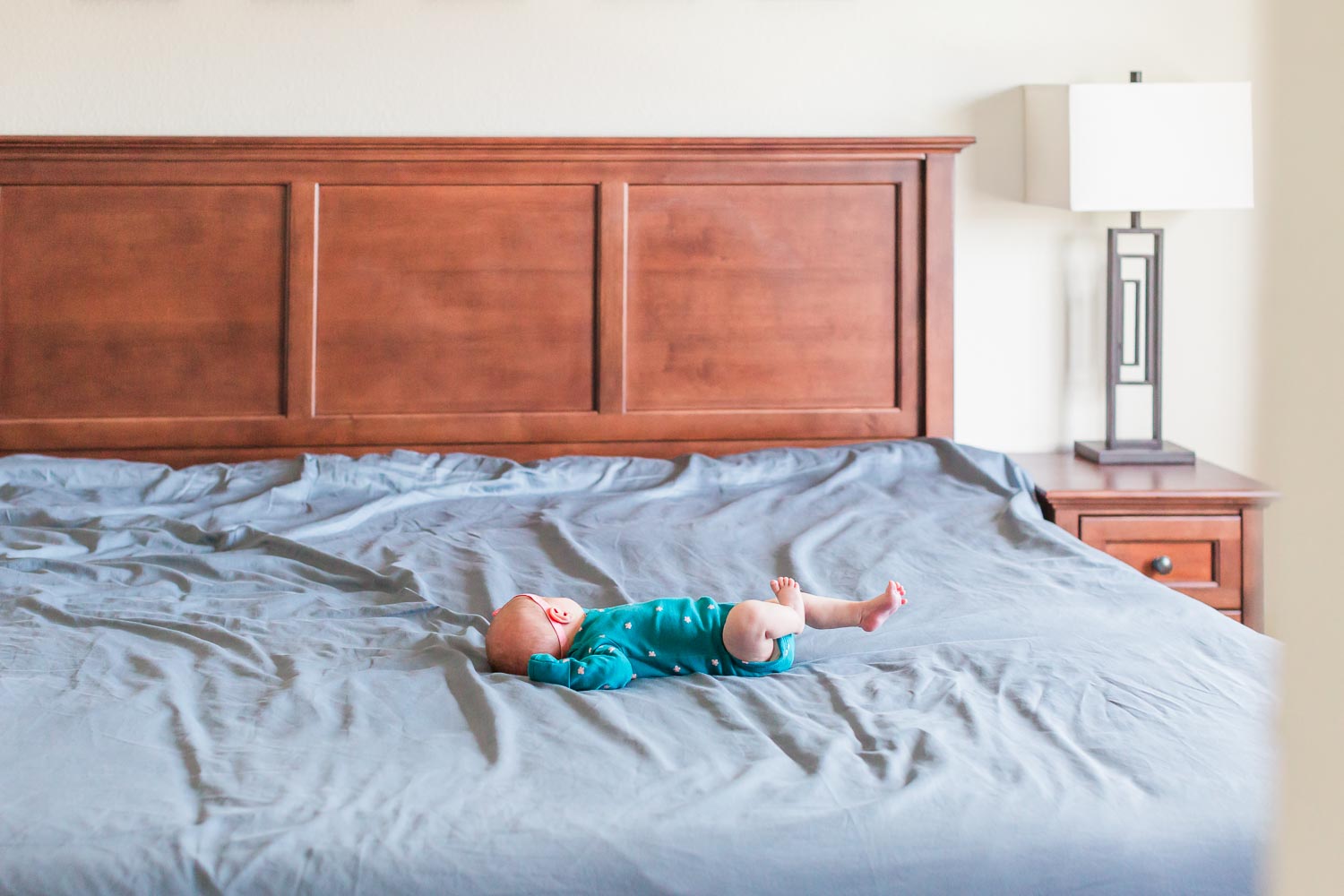 In-home newborn session in Erie, Colorado—newborn baby lying on a large bed with a wooden headboard, captured in a simple, natural moment. Photographed by Theresa Pelser, Erie newborn and family photographer.