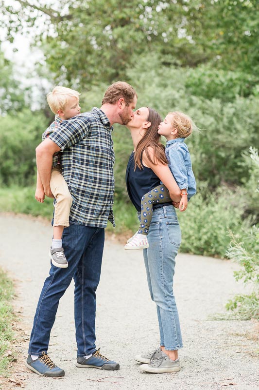 Family of four dressed in jeans and coordinated blues and greens for casual and relaxed outdoor family photos.