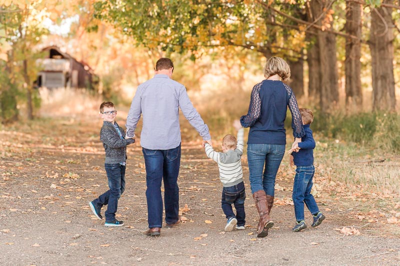 Family of five walking down a leaf-covered path wearing jeans layered with textured blues for outdoor family photos.