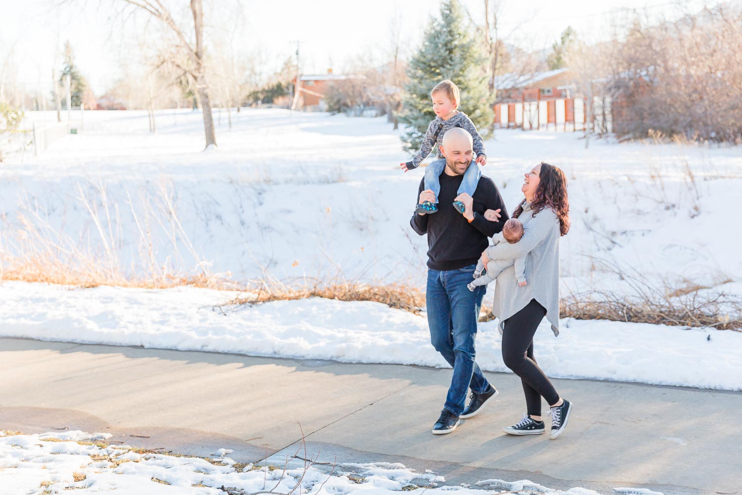 Winter family photo session in Boulder, Colorado with parents walking outdoors and carrying their toddler and newborn.