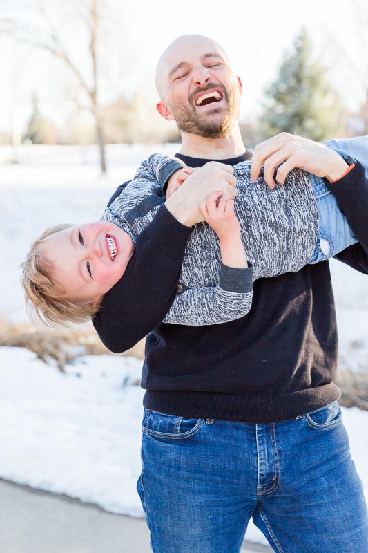 Dad laughing while holding his son upside down during outdoor family photos in Boulder, Colorado.