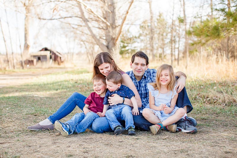 Family of five snuggle together in a field during outdoor family photos at the Wise Homestead— relaxed, natural smiles.