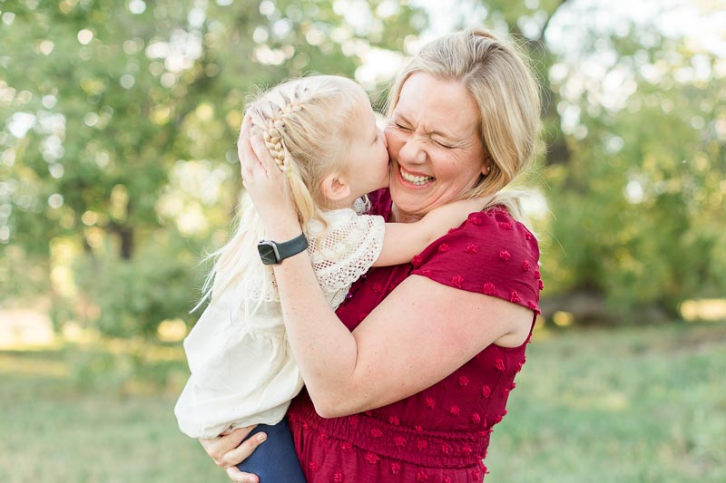Mom laughing while her young daughter kisses her cheek during outdoor family photos at Thomas Reservoir, in Erie, Colorado.