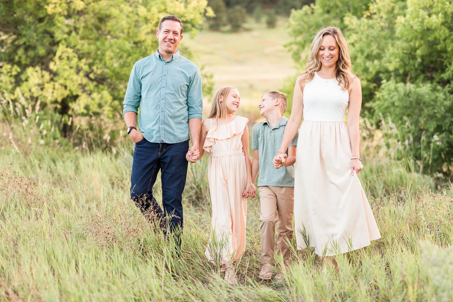 Family session at Chautauqua in Boulder, Colorado with mom, dad, and two children walking through a sunlit grassy field, natural and relaxed.