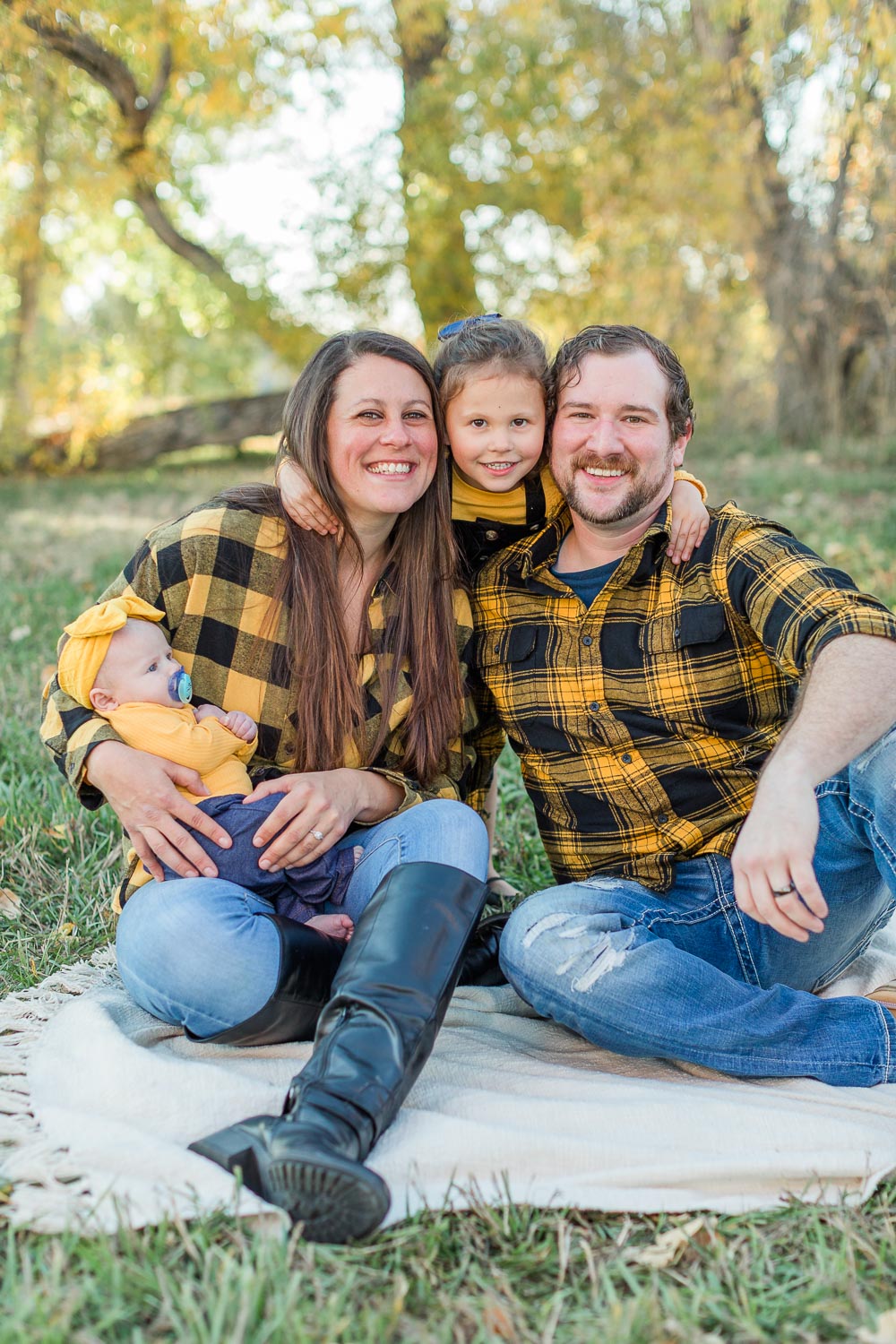 Outdoor fall mini session with parents and two children sitting together on a blanket, laughing and leaning into each other at Thomas Reservoir in Erie, Colorado