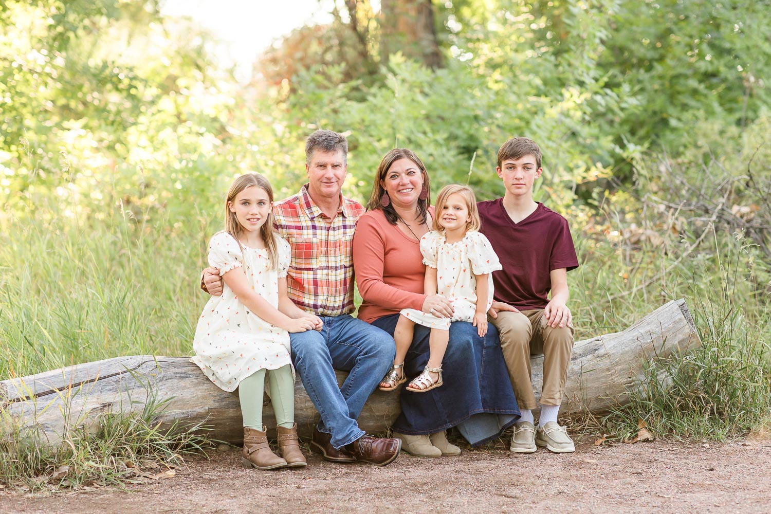 all mini family photography session with parents and three children sitting together on a log at McKay Lake near Erie, Colorado, smiling and leaning close