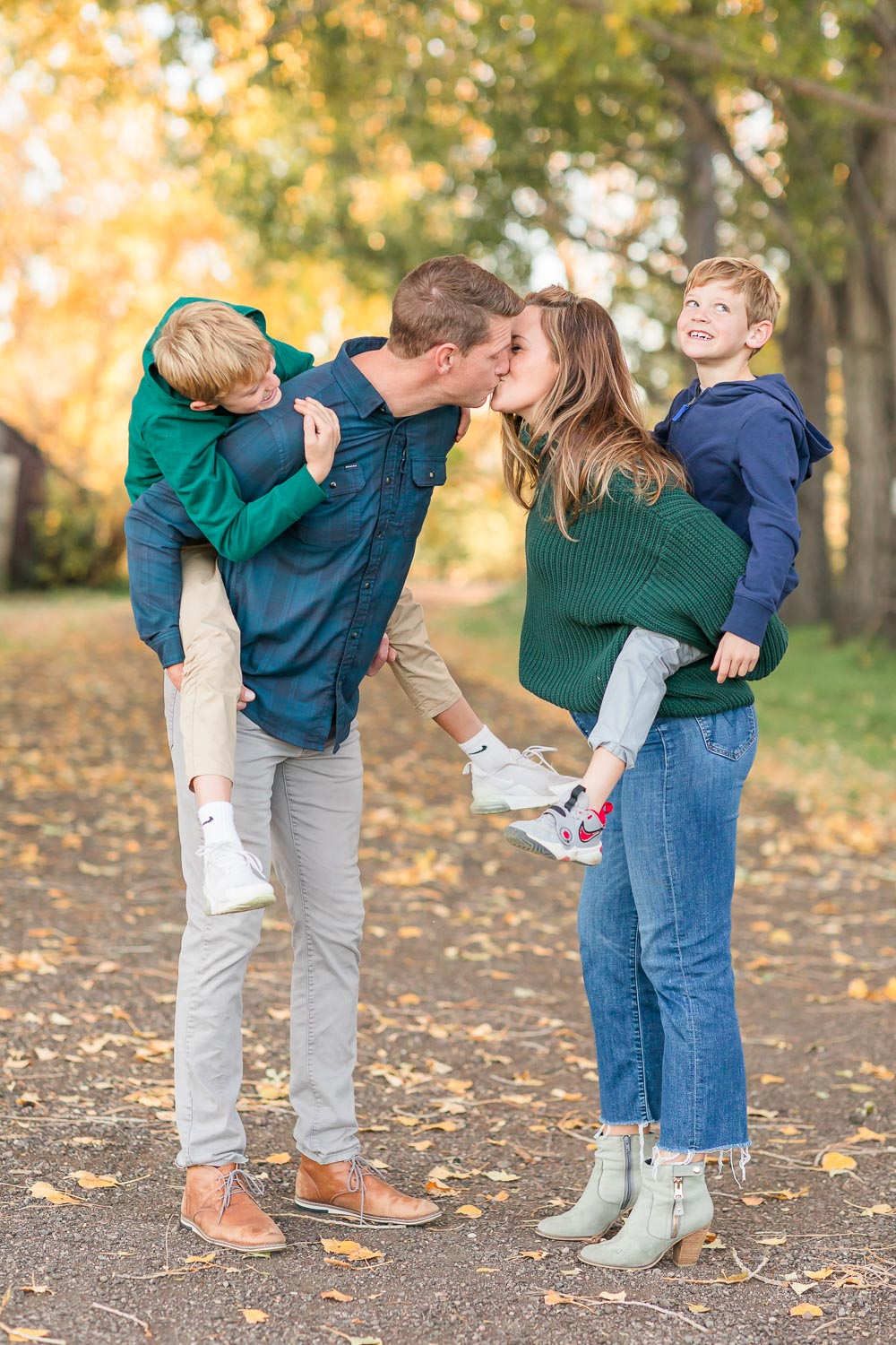 A mom and dad piggy backing their two young boys lean in for a kiss during their fall family session in Erie, Colorado