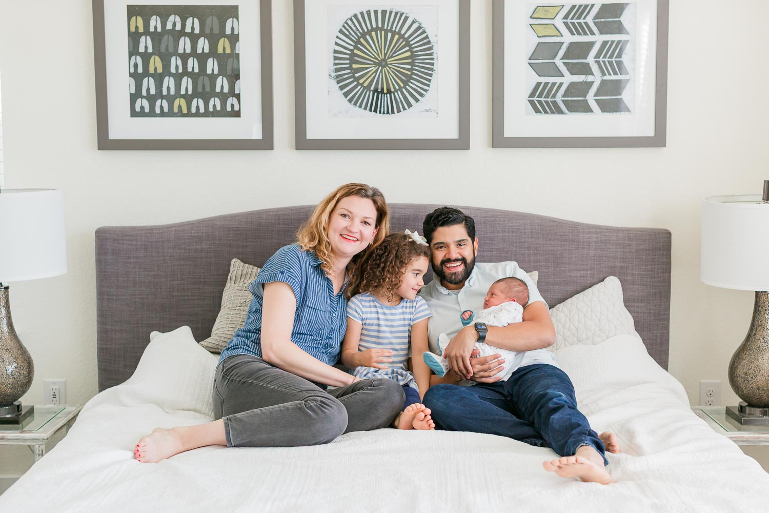 Lifestyle newborn photography session in Erie, Colorado with parents, big sister, and their newborn baby cuddled together on a bed, warm and natural in-home family photo.