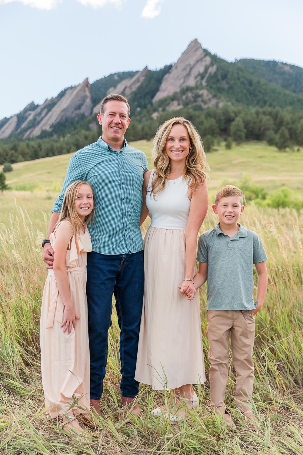 Family photography session at Chautauqua in Boulder, Colorado with mother, father, and two young children standing together in a grassy field, with the Flatirons in the background.