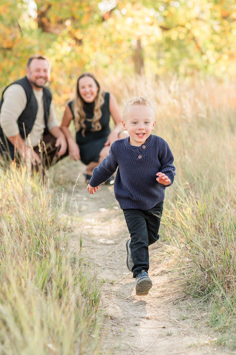 Young child running toward the camera while his parents stand behind him during outdoor family photos