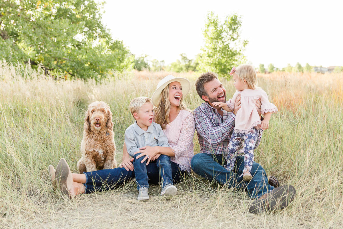 Family of four sitting close together in tall grass during an outdoor mini session